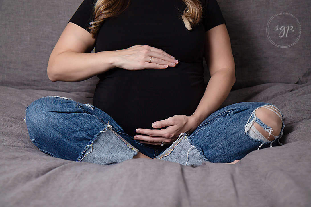 mama to be in jeans and black top sitting on her bed at indoor maternity photo session in Houston Texas, Houston maternity photographer