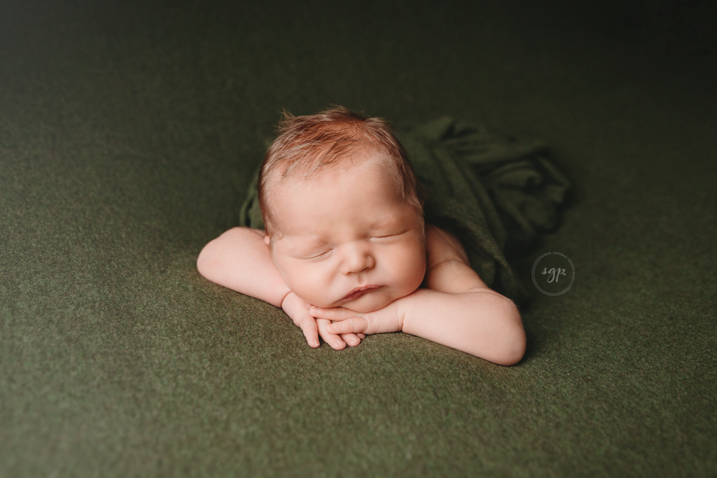 baby boy asleep on his hands on a dark green backdrop during his Houston in-home newborn photoshoot with Houston newborn photographer