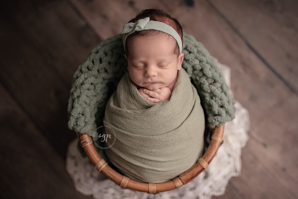 baby girl wrapped in sage with matching bow in a basket at newborn photoshoot in Houston, Texas