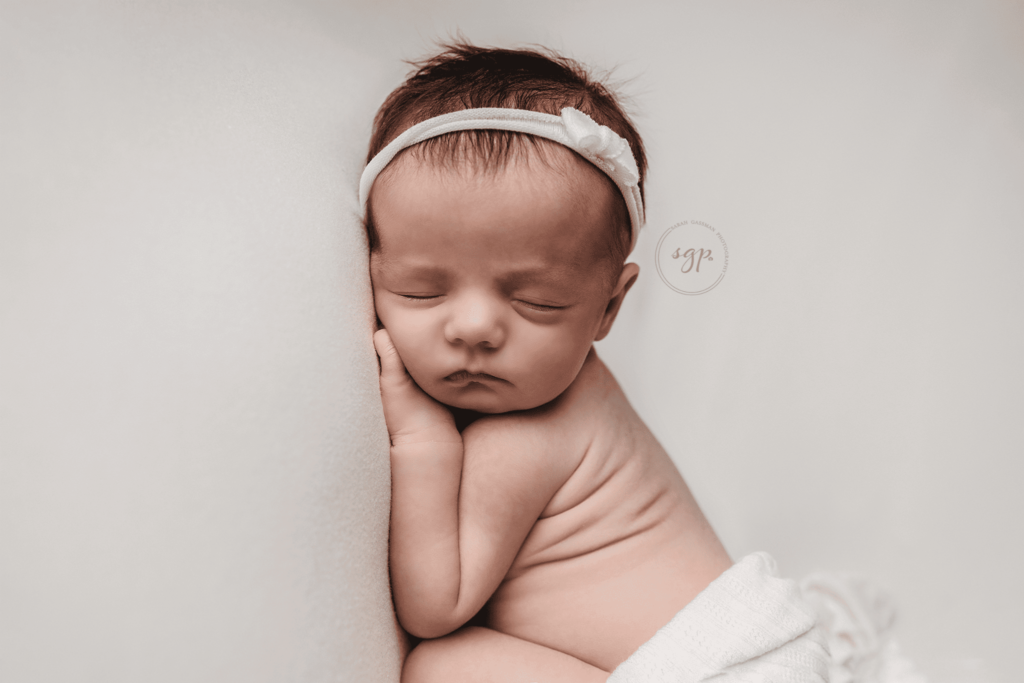 baby girl sleeping soundly wrapped in white with baby rolls showing