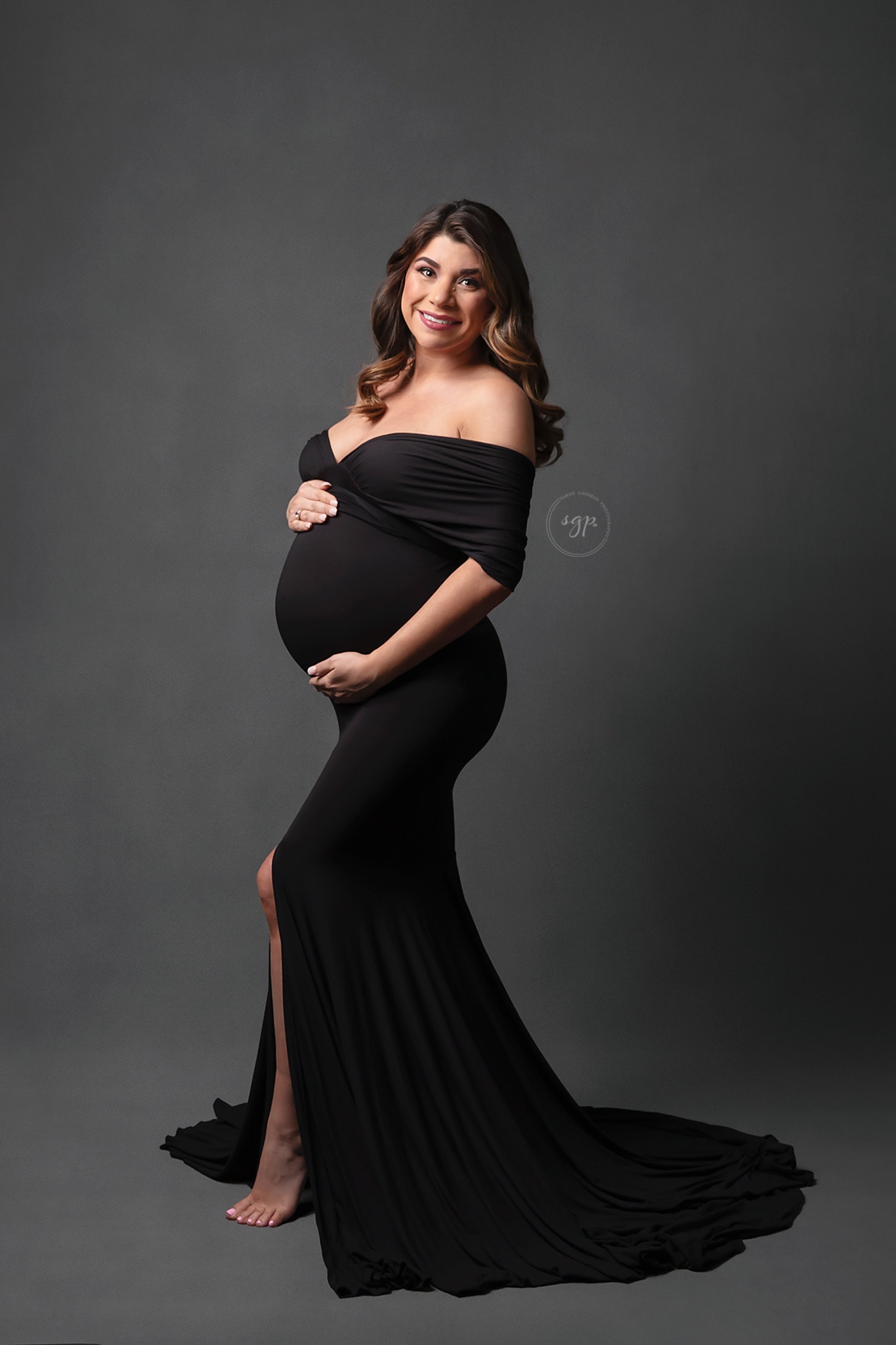 Expecting mother in long black dress with leg slit at indoor maternity photo session with Houston maternity photographer