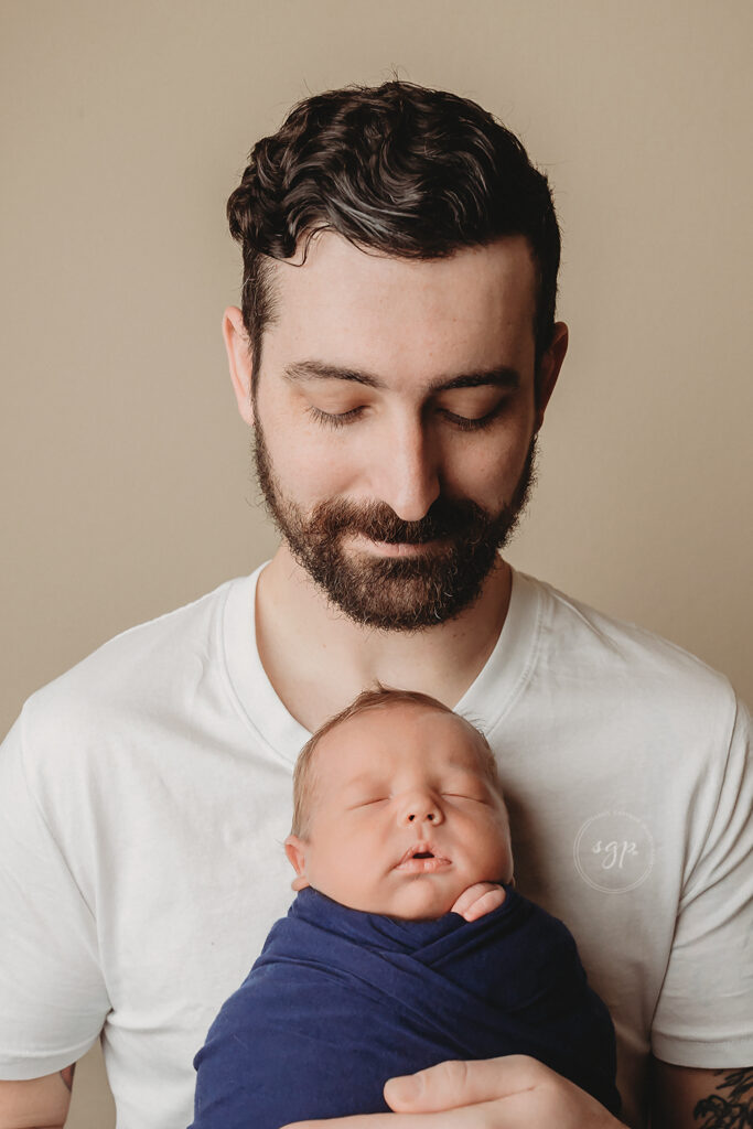 Dad proudly holds new baby boy and looks lovingly down at him at their Cypress in-home newborn photo session