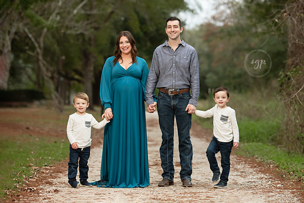 family with two boys holding hands on gravel road at Cypress outdoor maternity photoshoot with Houston maternity photographer