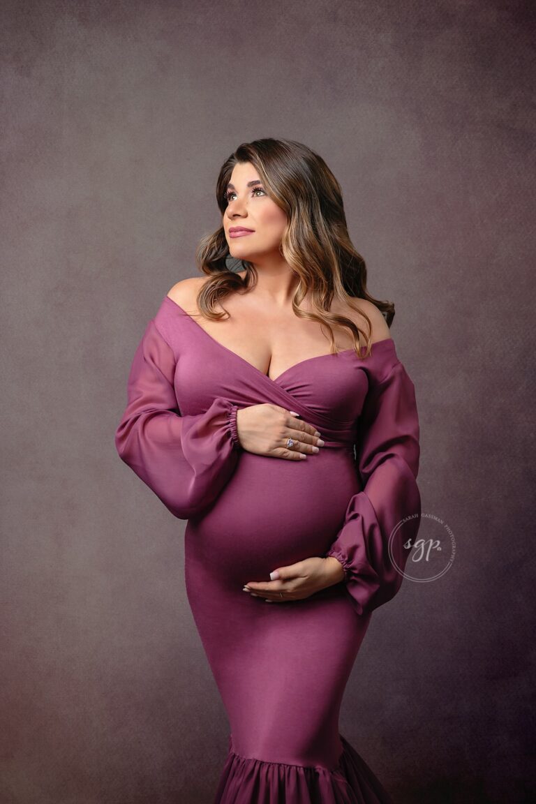 Three-quarter crop of a happy mama to be in mauve colored, mermaid style dress at indoor maternity photoshoot in Houston, Texas with Houston maternity photographer