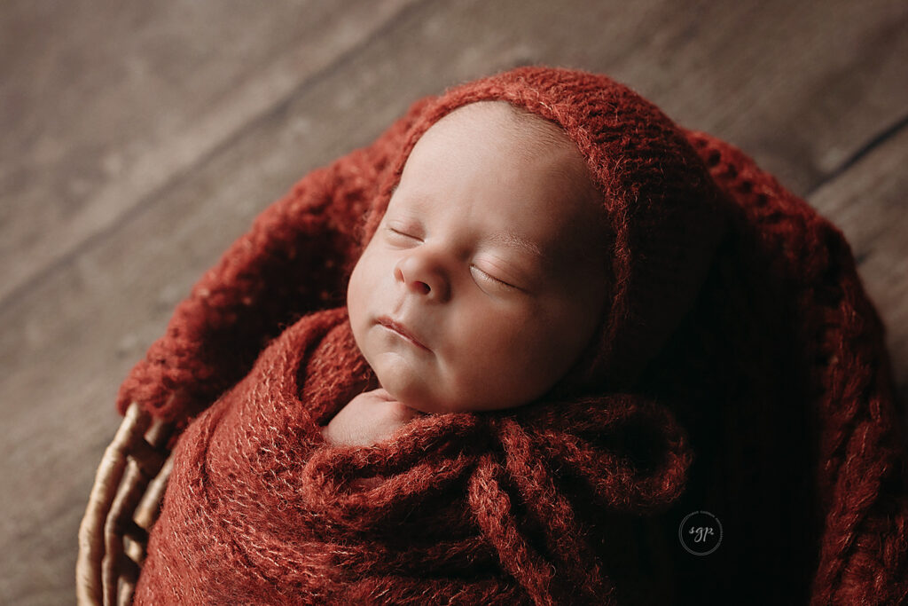 award-winning photo - baby boy wrapped in rust color knit with matching bonnet at in-home newborn photo session, Cypress TX newborn photographer