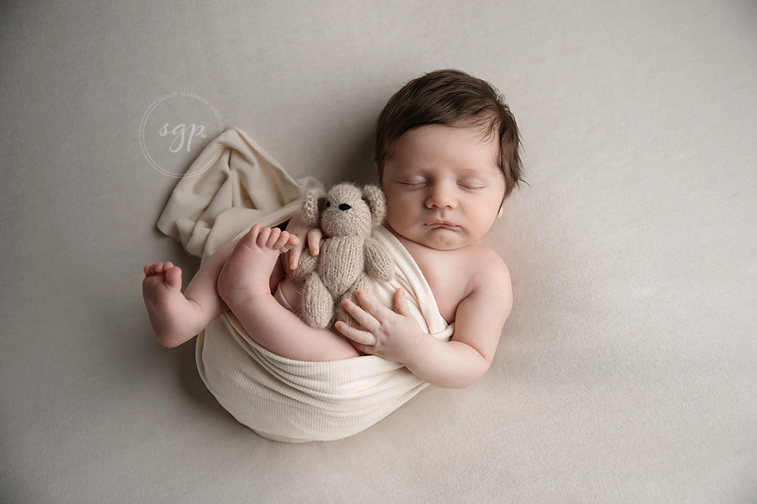 baby snuggling teddy bear while wrapped in cream colored wrap at in-home newborn photo session with Houston newborn photographer