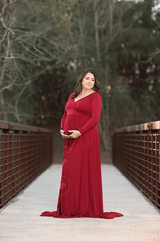 mama to be in long red dress on bridge at outdoor maternity photo session in Houston Texas, Houston maternity photographer