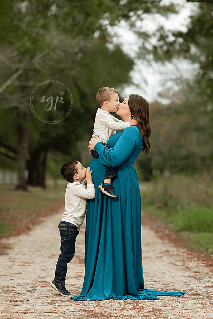 expecting mother with two boys on gravel road at Cypress outdoor maternity photoshoot with Houston maternity photographer