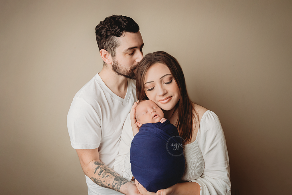 Dad kisses mom while holding newborn baby boy