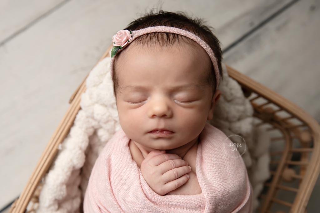 baby girl wrapped in pink with matching pink floral headband posed asleep in a wooden basked at her Houston in-home newborn photoshoot with Houston newborn photographer