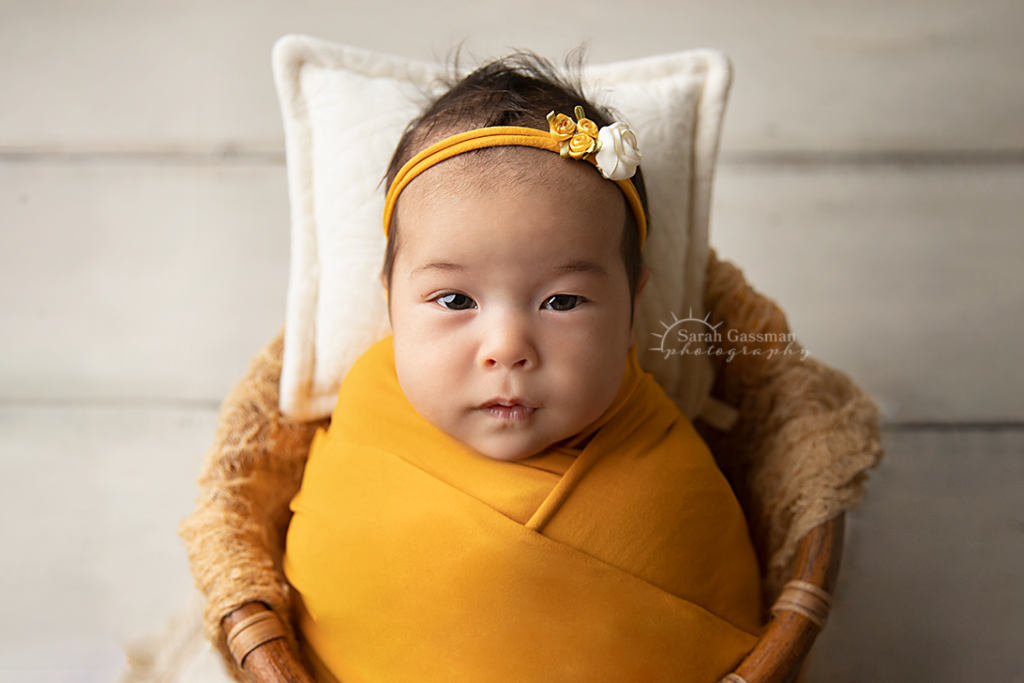 baby girl wrapped in yellow with matching headband posed awake in a cute basket during her Houston in-home newborn photo session with Houston newborn photographer
