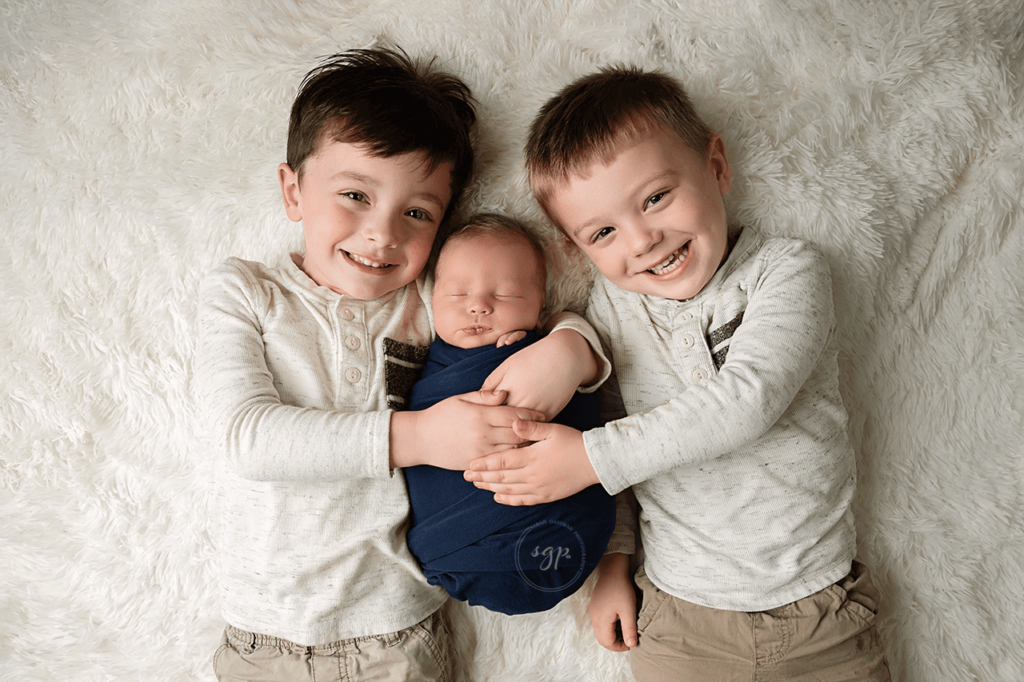 big brothers hold their new baby brother at his at-home newborn photo session in Cypress Texas, Houston newborn photographer