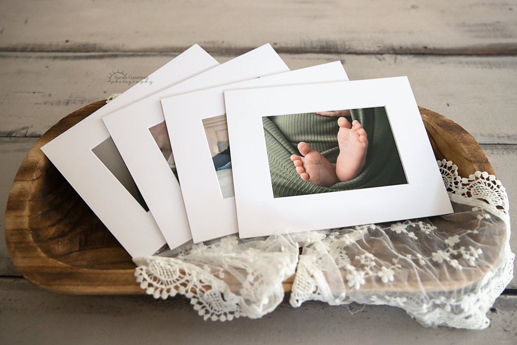 matted prints from newborn photos in a wooden bowl