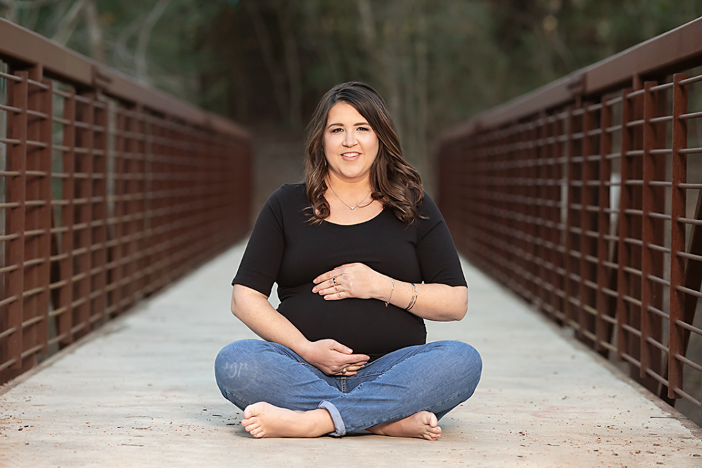 black and white picture of baby bump with mom to be sitting on a bridge at outdoor maternity photo session. Houston Texas maternity photographer