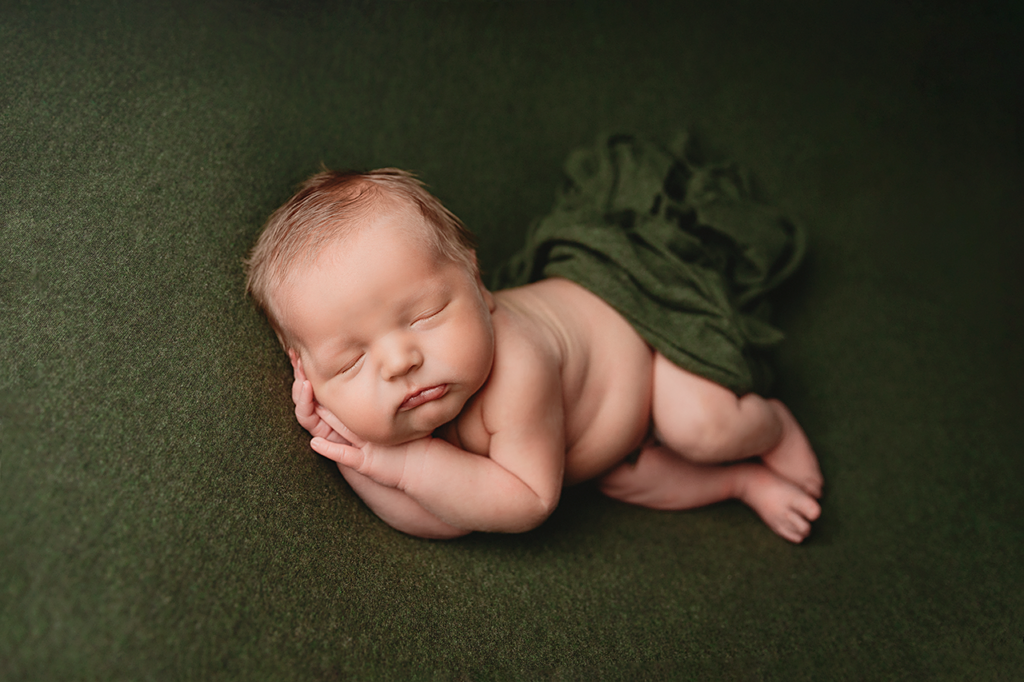 baby boy sleeping on his side on a dark green backdrop at in-home newborn photo session in Houston
