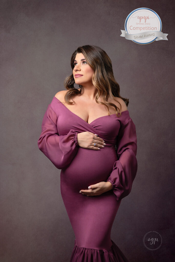 international award-winning photo of an expecting mother in a dark pink gown and a matching textured backdrop looking up thinking about her soon to be baby taken at her in-home maternity photo session by Houston maternity photographer