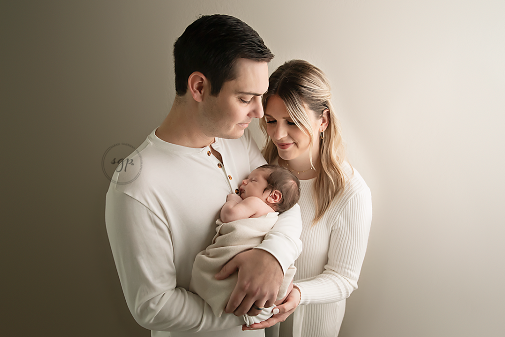 parents show love and bonding while holding their new baby while all dressed in cream colors at their in-home Houston newborn photo session.
