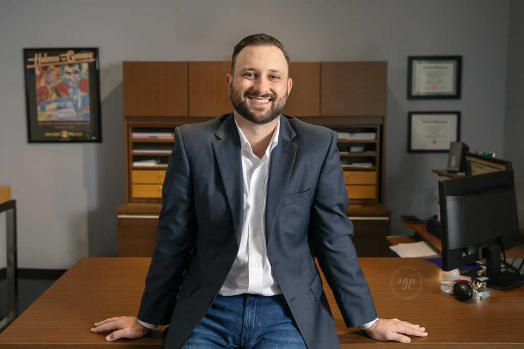 man smiling while sitting on desk at in-office branding photo session with Houston headshot photographer