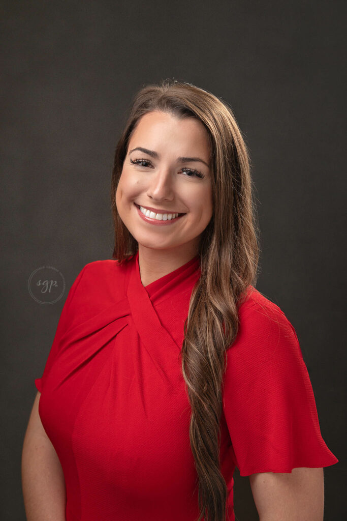 corporate headshot of woman in red top with long brown hair and a glowing smile