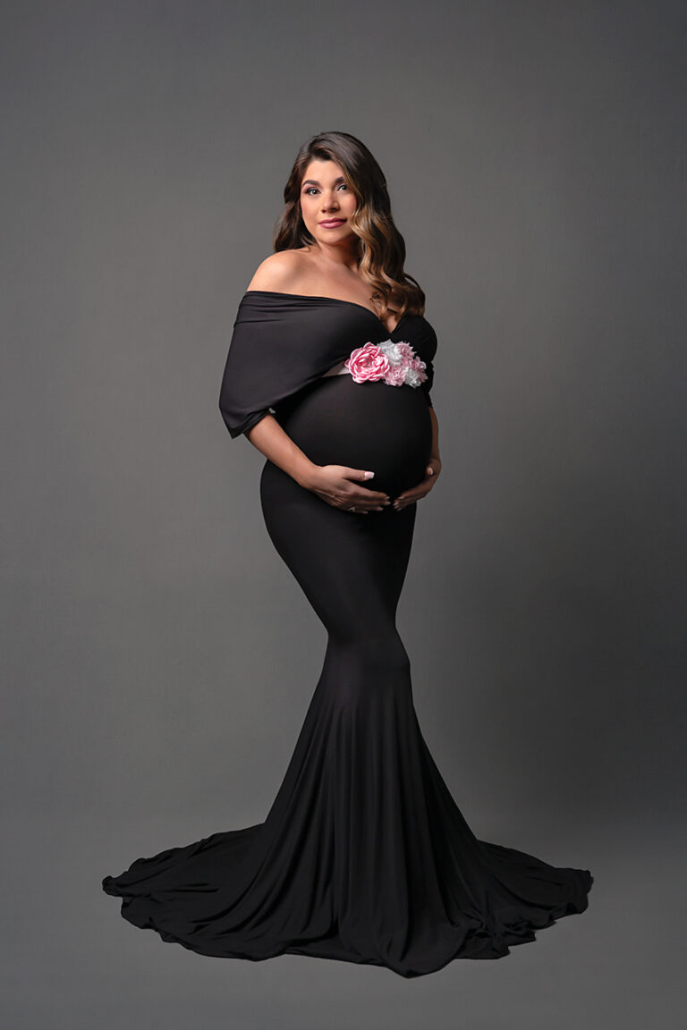 Expecting mother in long black dress with leg slit at indoor maternity photo session with Houston maternity photographer