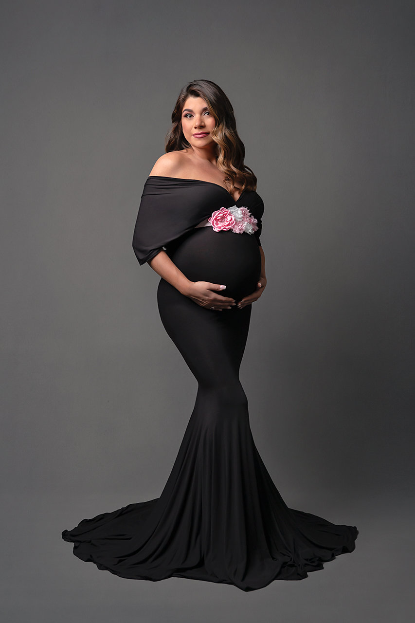 Expecting mother in long black dress with leg slit at indoor maternity photo session with Houston maternity photographer