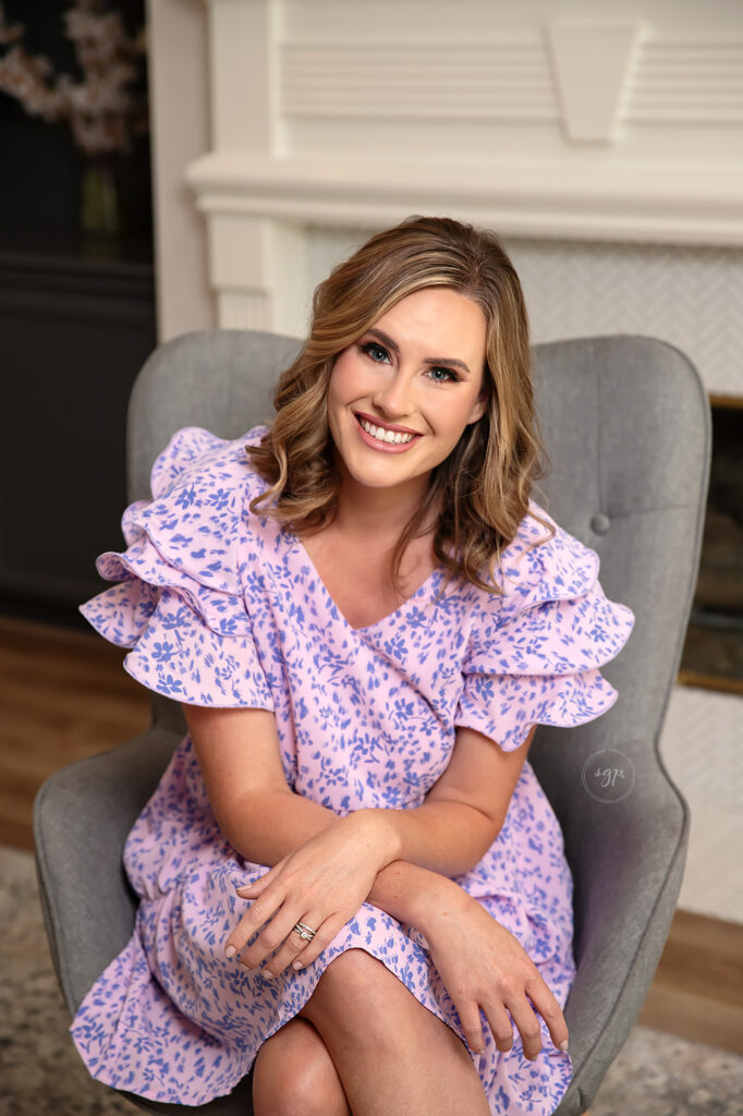 woman wearing purple floral dress sitting in gray chair in modern headshot