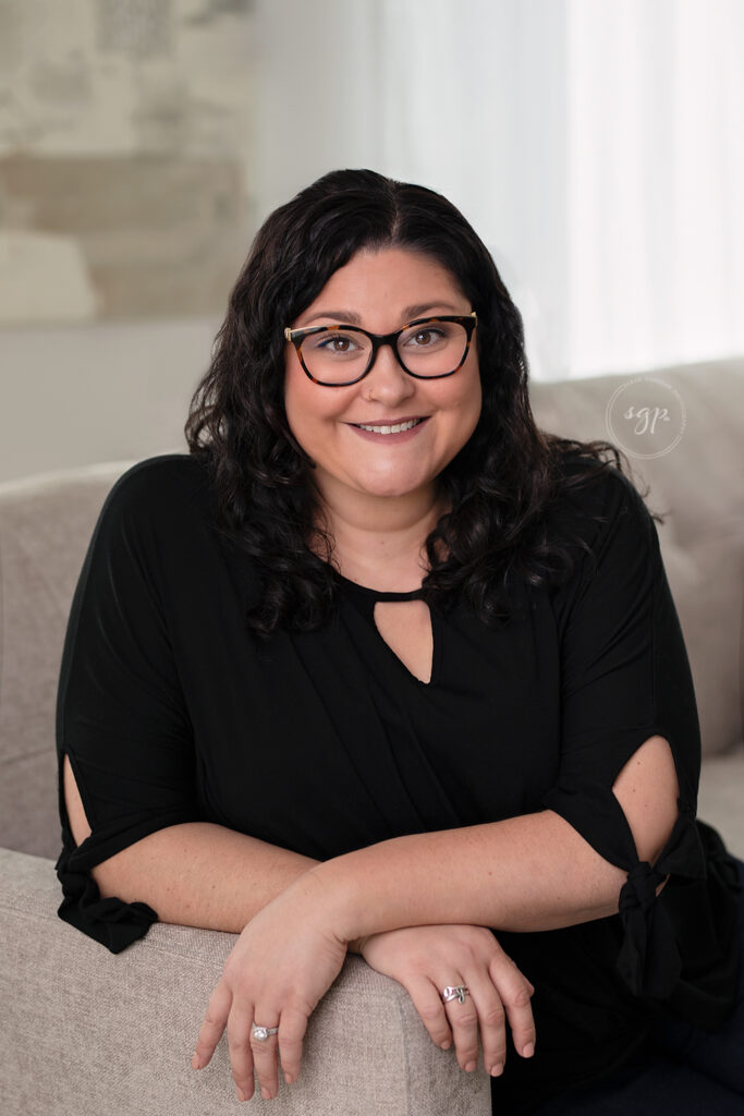 modern headshot of woman in black top sitting on couch with glasses