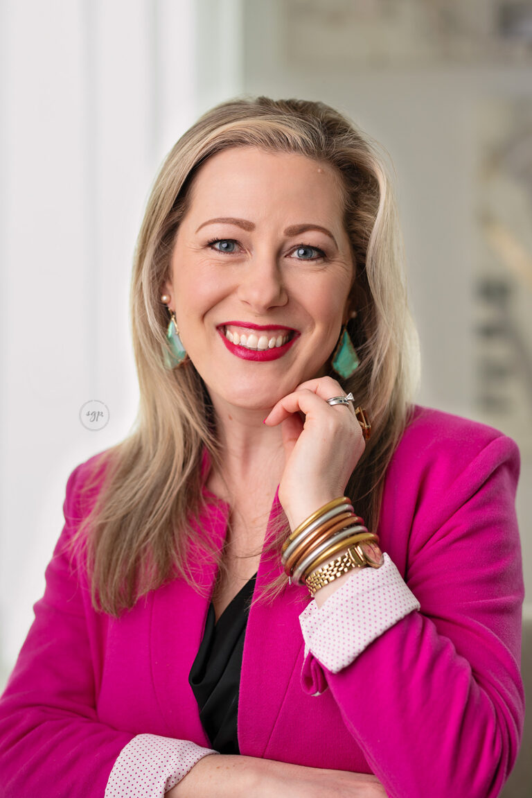 woman wearing bright pink jacket with black shirt and lots of jewelry posed in a modern headshot