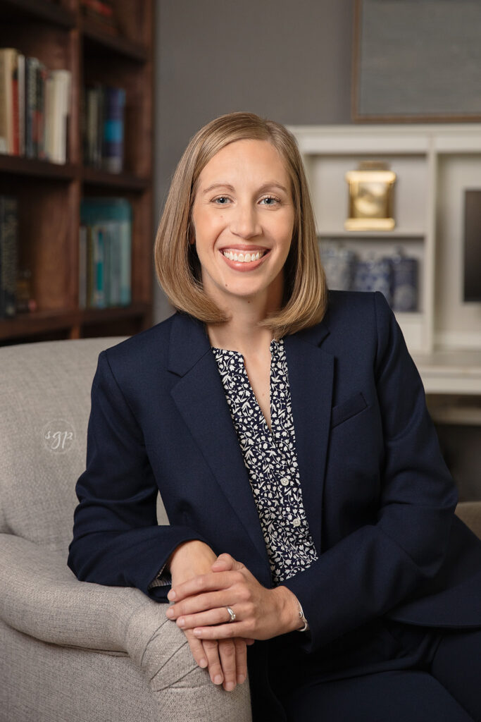 woman wearing navy blazer sits on gray armchair in office for lifestyle headshot